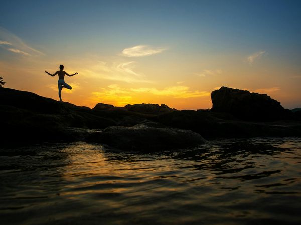Silhouette of a person in a yoga warrior pose against a vibrant sunrise, symbolizing energy and strength.